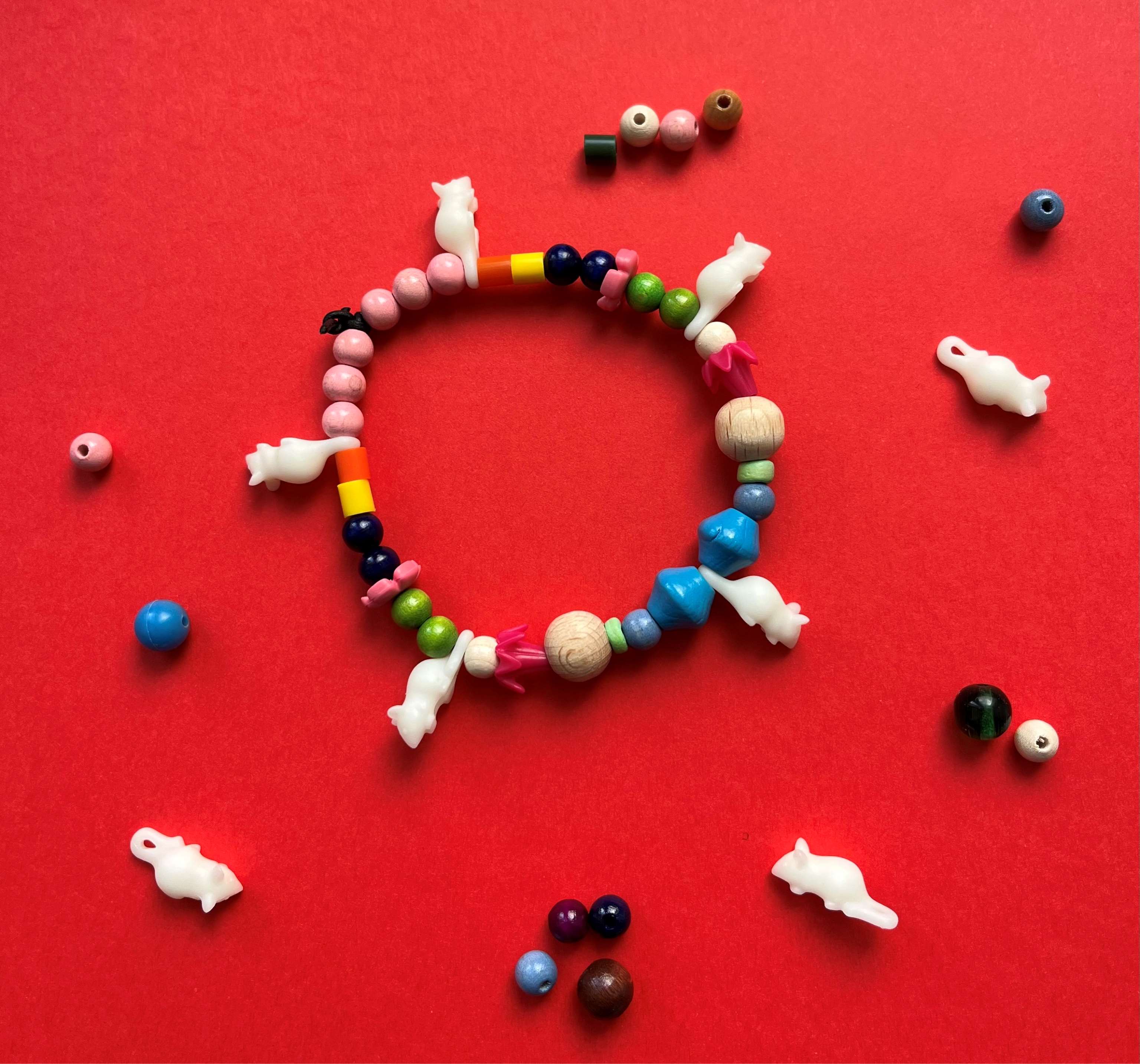 Foto zum Osterferienprogramm. Zu sehen ist ein Armband aus unterschiedlichen Perlen und fünf weißen PLAYMOBIL-Mäusen.