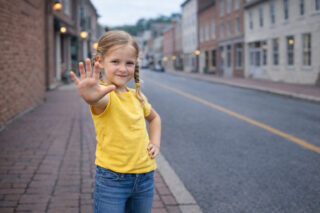 Mädchen in einem gelben T-Shirt, das selbstbewusst die Hand in einer "Stopp"-Geste ausgestreckt hat.
