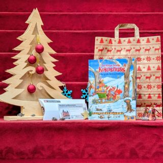 Weihnachtspaket: Buch "Der kleine Drache Kokosnuss. Das große Weihnachtsbuch", Generationenkarte für die Sonderausstellung "Der kleine Drache Kokosnuss", Geschenktüte und weihnachtliche Dekoration.