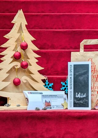 Weihnachtspaket: Ausstellungskatalog "Horst Hamann – Kaiserdom zu Speyer. Vertical Photographs", Generationenkarte für die Sammlungsausstellung "Kreuz und Krone", Geschenktüte und weihnachtliche Dekoration.