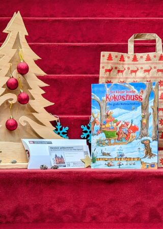 Weihnachtspaket: Buch "Der kleine Drache Kokosnuss. Das große Weihnachtsbuch", Generationenkarte für die Sonderausstellung "Der kleine Drache Kokosnuss", Geschenktüte und weihnachtliche Dekoration.